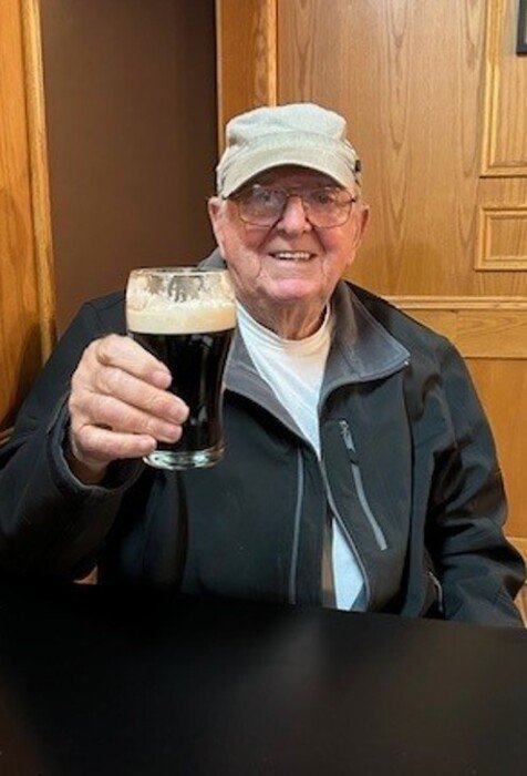 Elderly man holding a glass of dark beer.