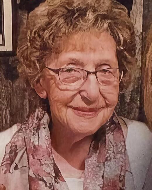 Elderly woman smiling with glasses and floral scarf.