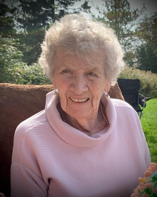 Smiling elderly woman outdoors with trees behind her.