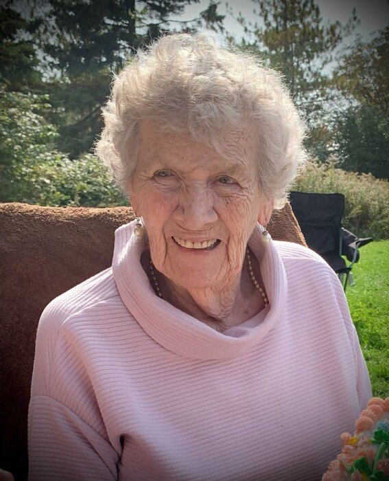 Smiling elderly woman outdoors with trees behind her.