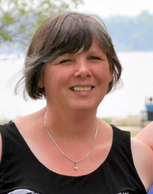 Smiling person outdoors by a lake.