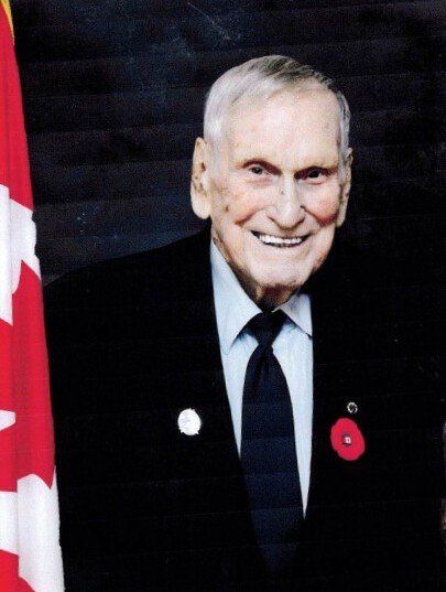 Elderly man smiling beside Canadian flag.