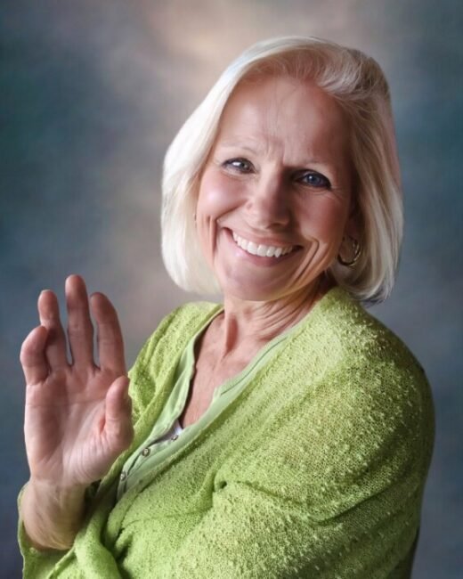 Smiling woman waving, wearing green sweater.