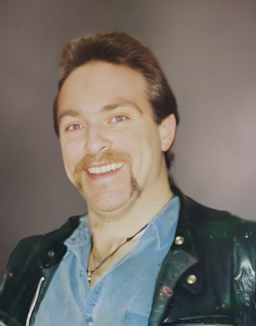 Smiling person with mustache and blue shirt.