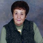 Elderly woman wearing a vest and green shirt.