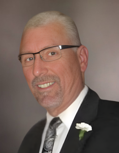 Man in suit with glasses and flower boutonniere.