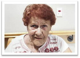 Elderly woman smiling in embroidered blouse indoors.