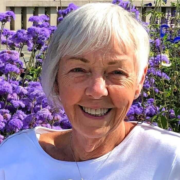BULL, Dorothy Bull Smiling woman with gray hair and purple flowers