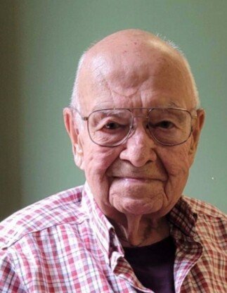 Elderly man wearing glasses and plaid shirt smiling.
