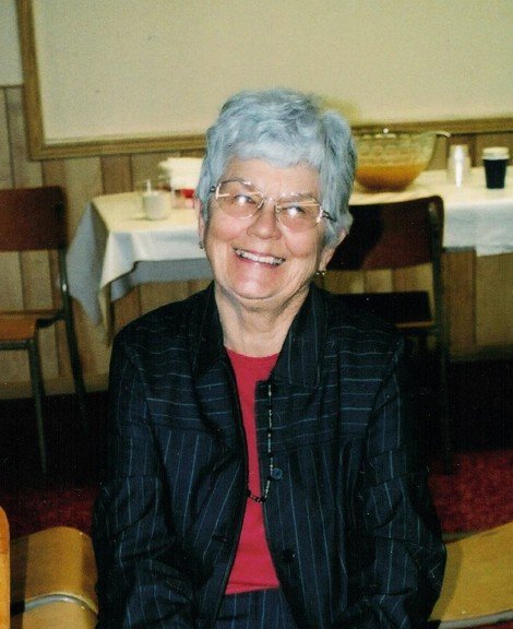 Smiling elderly woman sitting at a dining table.