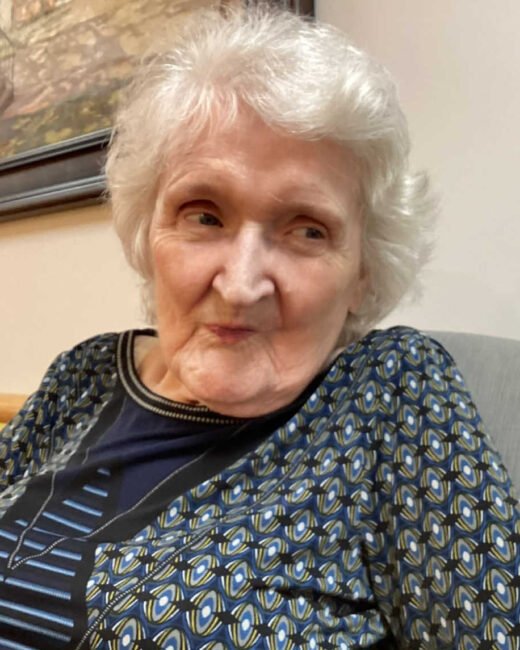 Elderly woman smiling indoors, patterned blouse.