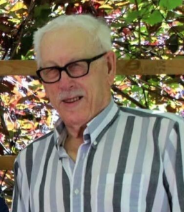Elderly man with glasses and striped shirt outdoors.