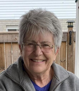 Smiling elderly woman with short gray hair outdoors.