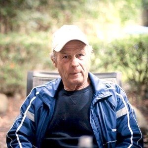 Man in blue jacket sitting in outdoor setting.