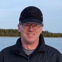 Smiling person wearing a black cap by the water.