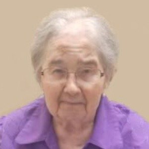 Elderly person wearing purple shirt, neutral background