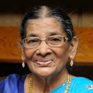 Elderly woman smiling, wearing glasses and earrings.