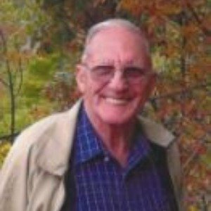 Smiling man outdoors surrounded by autumn leaves.