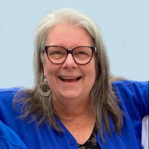 Smiling person with glasses and gray hair in blue