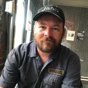 Man wearing Jeep cap indoors, seated at table.
