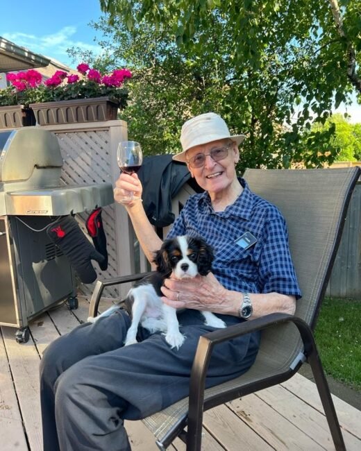 Man with puppy on porch, holding wine glass.