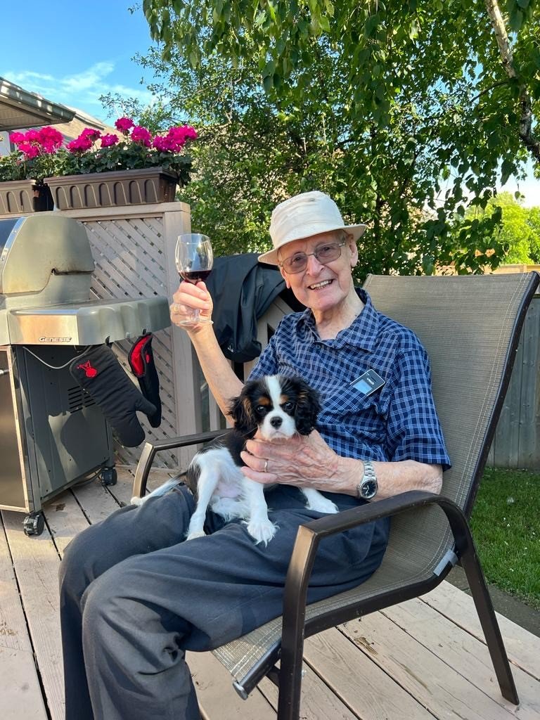 Man with puppy on porch, holding wine glass.