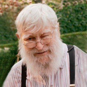 Elderly man with beard smiling outdoors.
