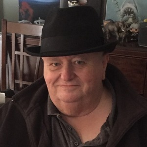 Man smiling, wearing black hat indoors.
