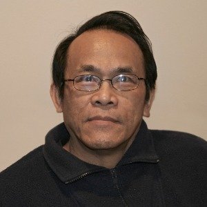 Person wearing glasses, dark jacket, neutral expression.