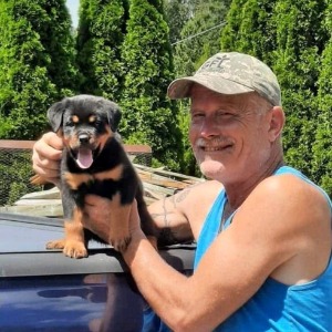 Man holding a happy Rottweiler puppy outside.