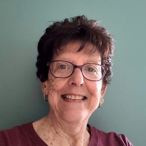 Smiling woman with glasses against green wall.