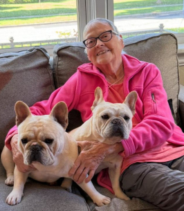 KIMPSON, Joan Marie Kimpson Smiling woman with two French bulldogs on couch.