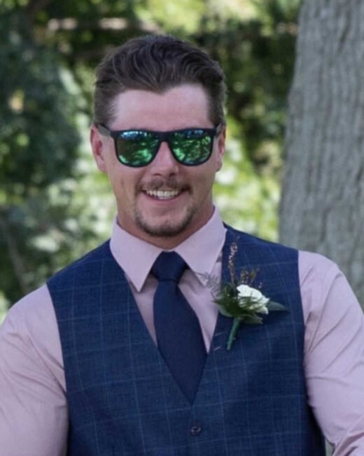 Smiling man in sunglasses and formal attire outside.