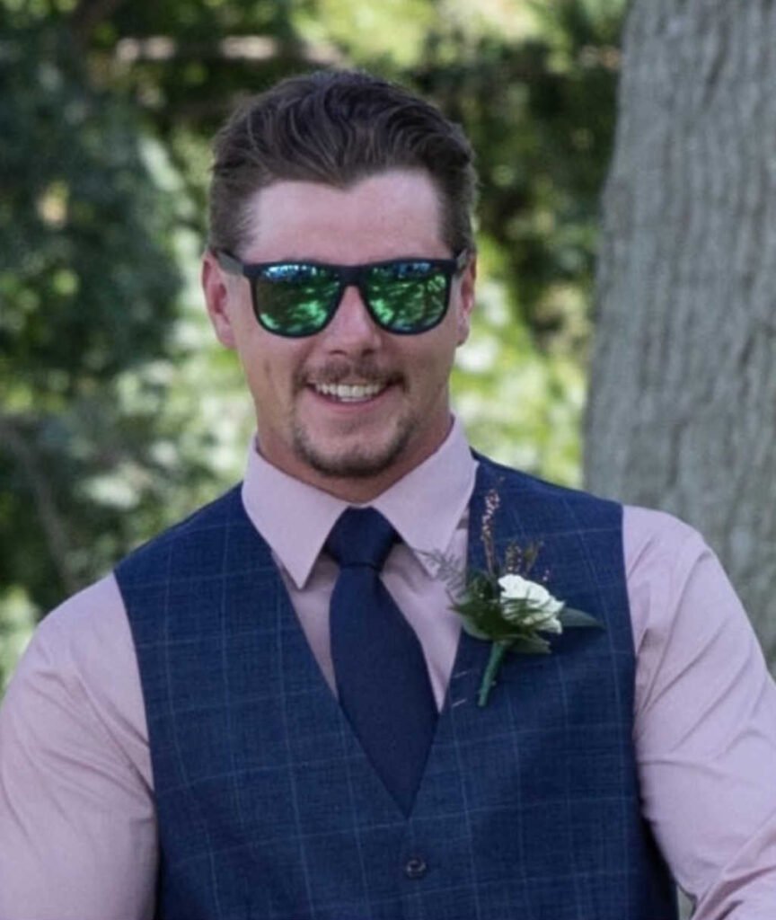 Smiling man in sunglasses and formal attire outside.