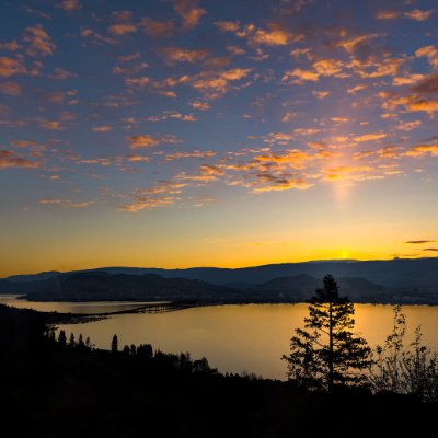 Sunset over lake with silhouetted trees and mountains.