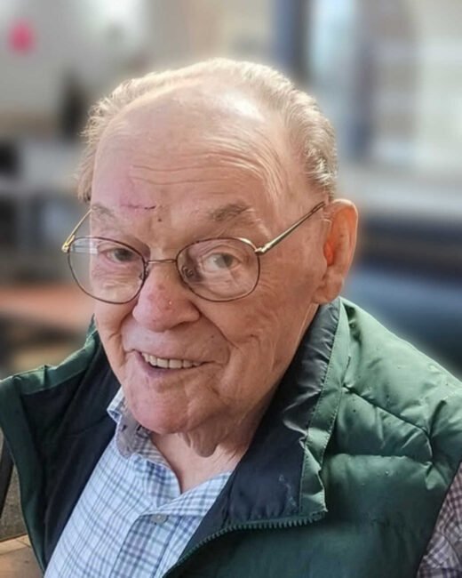 Elderly man smiling with glasses and green jacket.