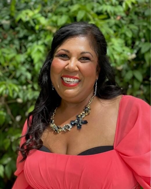 Smiling woman in pink dress and floral necklace.