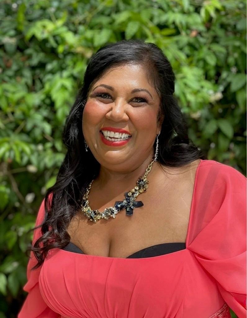 Smiling woman in pink dress and floral necklace.