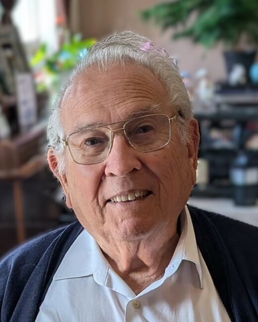 Elderly man smiling indoors, wearing glasses.