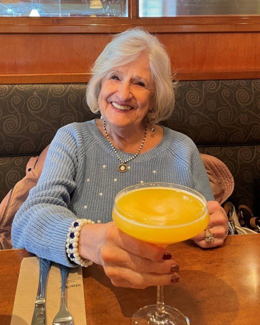 Smiling woman holding an orange cocktail at restaurant.