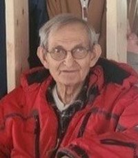 Elderly man smiling, wearing red jacket indoors.