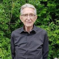 Elderly man smiling in front of green foliage.
