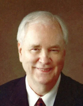 Smiling man in suit with gray hair.