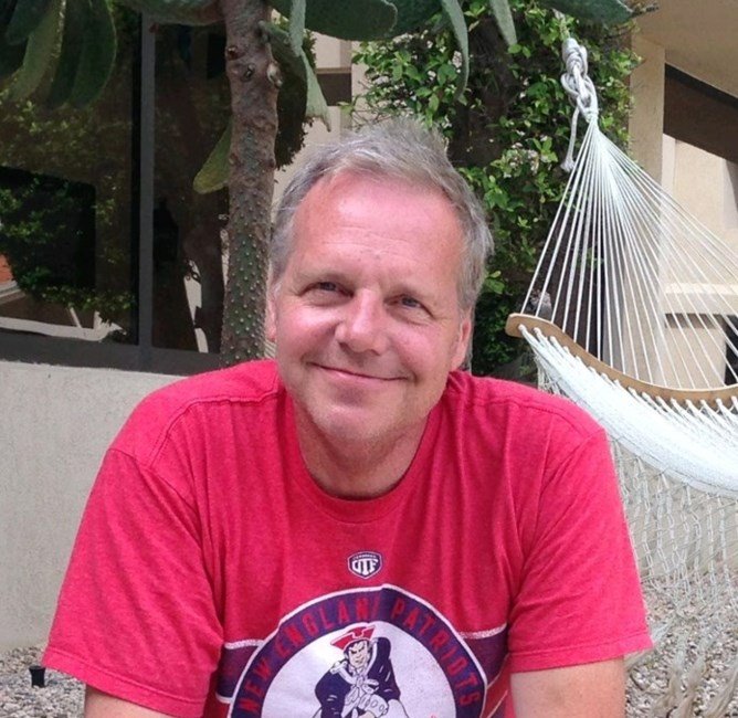 Man smiling outdoors in a red shirt.