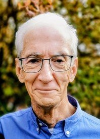 Elderly man in glasses and blue shirt smiling.