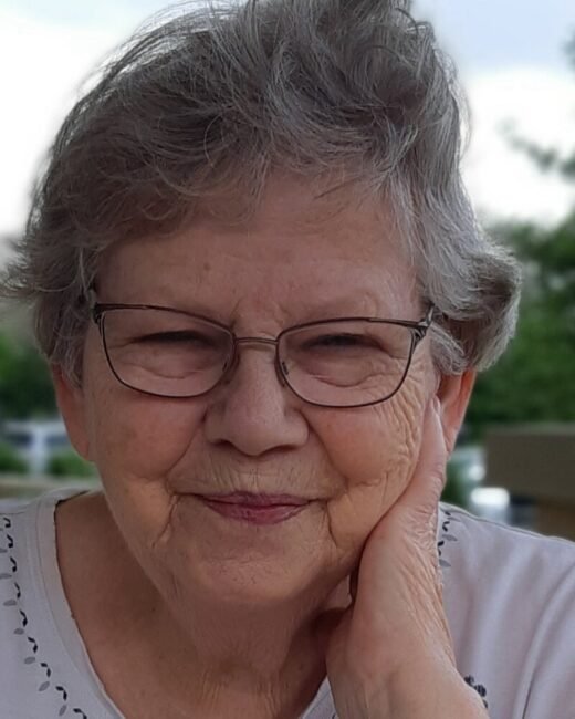 Smiling elderly woman with glasses outdoors.