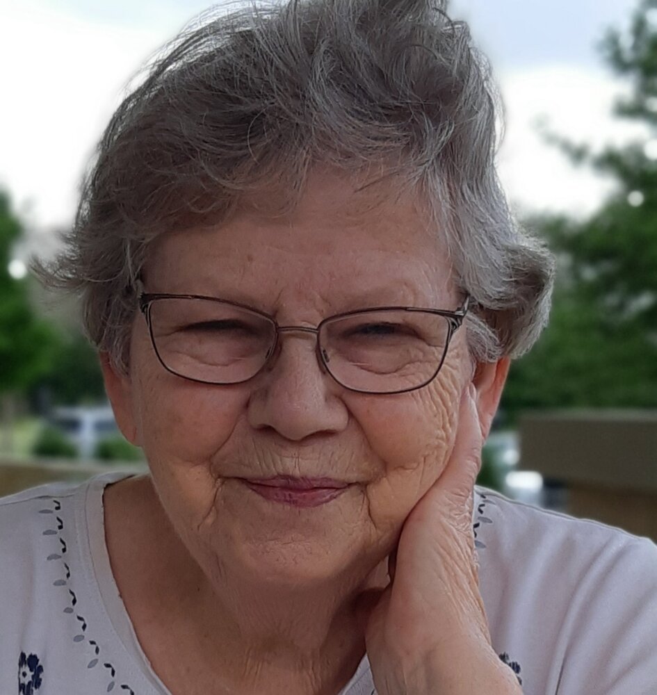 Smiling elderly woman with glasses outdoors.