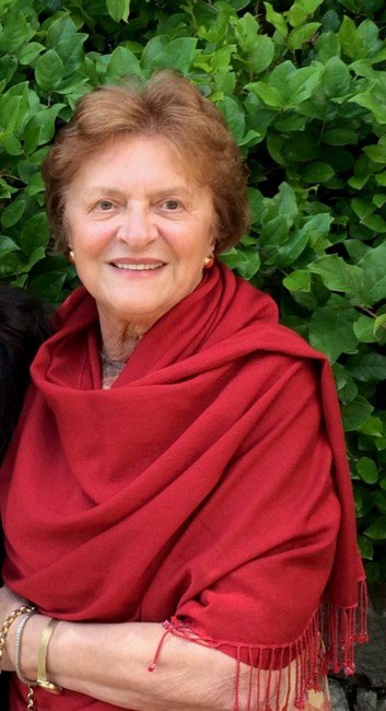 Smiling woman in red shawl, green foliage background.