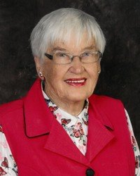 Smiling elderly woman wearing glasses and red vest.