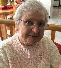 Elderly person smiling indoors with glasses and sweater.